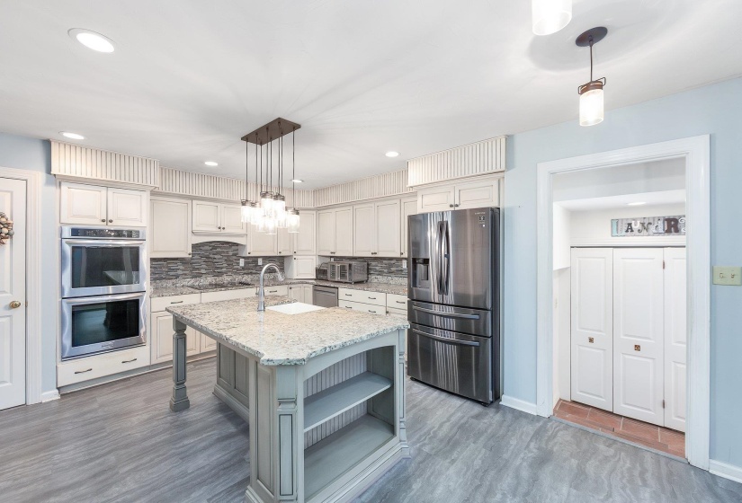 Kitchen with a kitchen island with sink, stainless steel appliances, a sink, backsplash, and open shelves