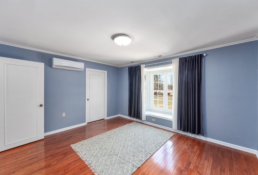 Empty room featuring wood-type flooring, crown molding, baseboards, and an AC wall unit