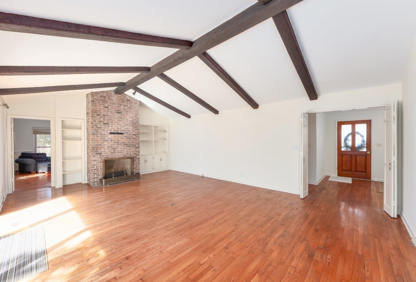 Living room with lofted ceiling with beams, light wood-style floors, a brick fireplace, and a healthy amount of sunlight