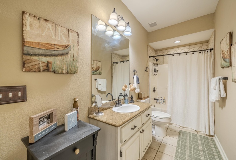 Bathroom featuring a single vanity with granite-finish countertop, white undermount sink, and a multi-bulb vanity light fixture