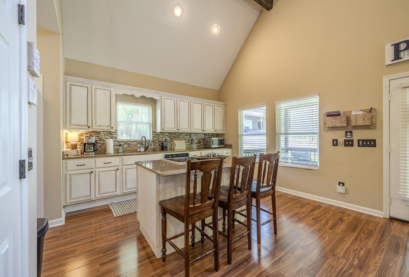 Kitchen featuring white cabinetry, a stone-finish countertop island, wood-finish flooring, a vaulted ceiling with exposed beam, and multiple windows with blinds