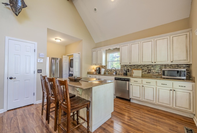 Kitchen featuring a vaulted ceiling, wood-finish flooring, a granite-topped island with seating, white cabinetry, and stainless steel appliances