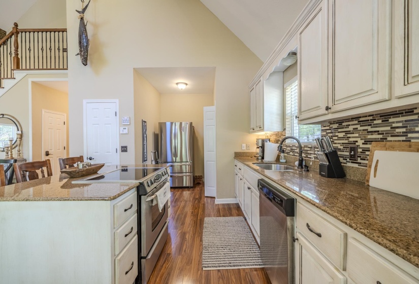 Kitchen featuring an island with a built-in cooktop, stainless steel appliances, granite countertops, and wood-finish flooring