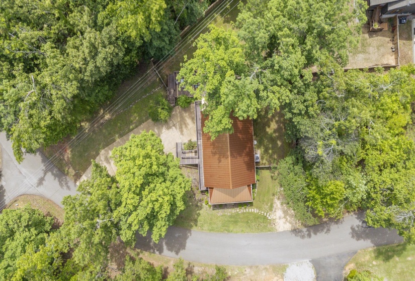 Terracotta-tiled roof structure surrounded by mature trees, featuring a gravel driveway and paved access roads