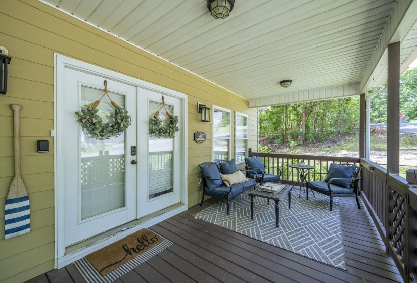 Covered porch featuring wood-finish flooring, white double French doors with glass panels, and a wood railing with lattice detailing