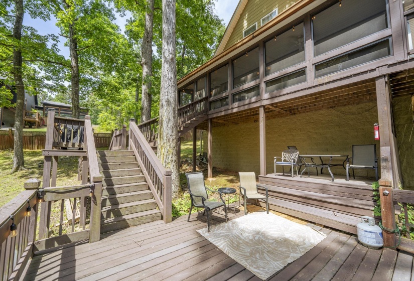 Multi-level wood-finish decking featuring a screened-in porch with clear panels, exterior stairs, and shaded outdoor living areas