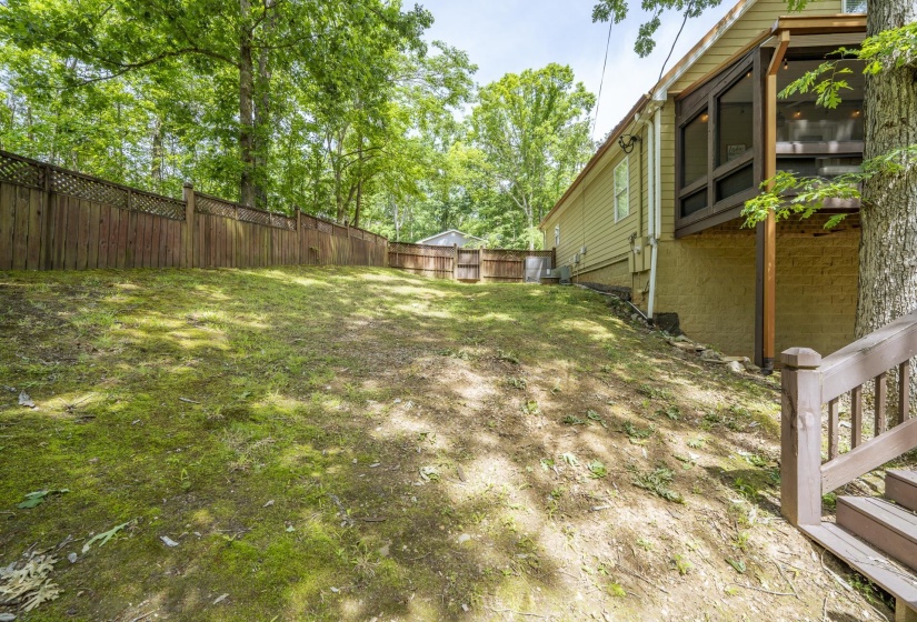Expansive sloped backyard featuring mature trees and a full privacy fence