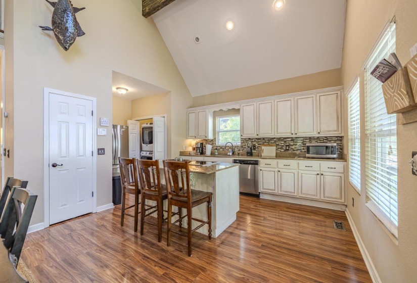 Kitchen featuring a central island with countertop seating, white cabinetry, a tile backsplash, stainless steel appliances, and wood-finish flooring