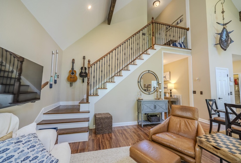 Two-story living area featuring a prominent staircase with wood treads and wrought iron balusters, high vaulted ceiling with exposed wood beam, wood-finish flooring, and recessed lighting