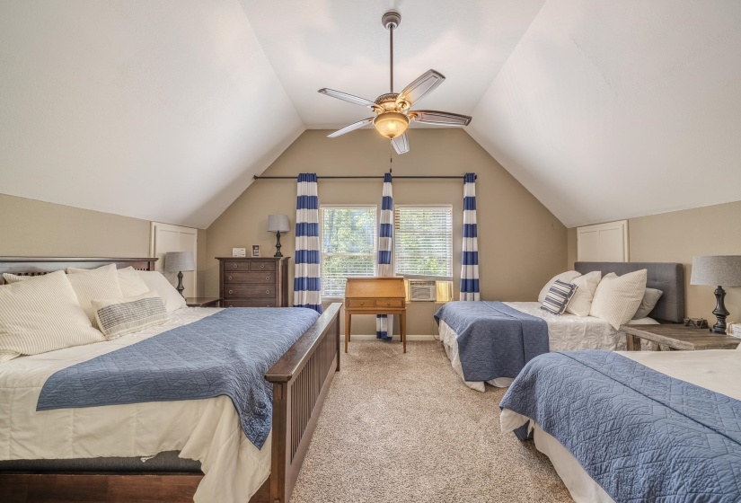 Spacious room featuring sloped ceilings, a ceiling fan with integrated lighting, window blinds, and light brown carpeting