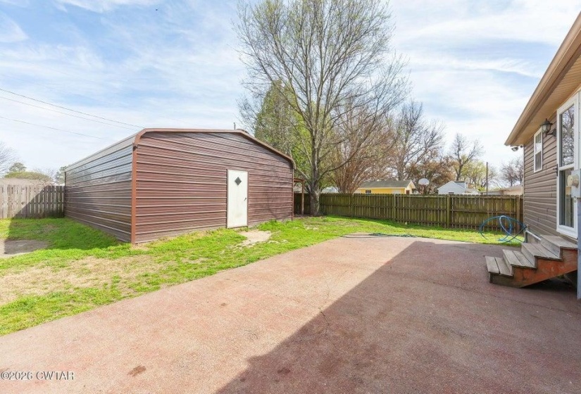 Fenced backyard featuring an outbuilding and a patio area