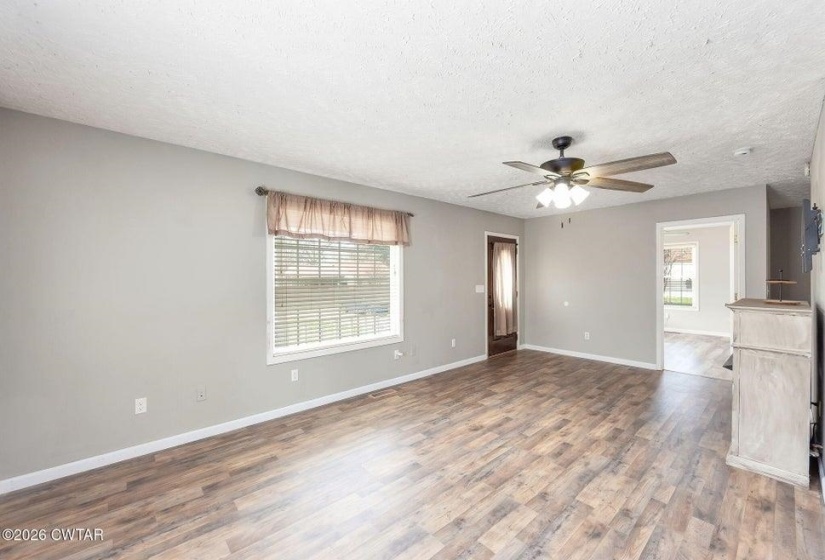 Unfurnished living room featuring dark wood-style floors, healthy amount of natural light, ceiling fan, and a textured ceiling