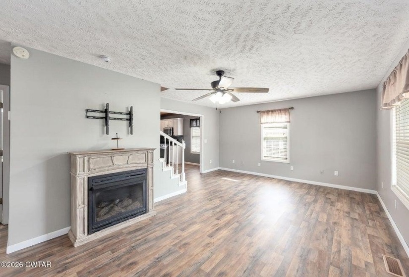 Unfurnished living room featuring a ceiling fan, dark wood-style floors, a textured ceiling, and a glass covered fireplace