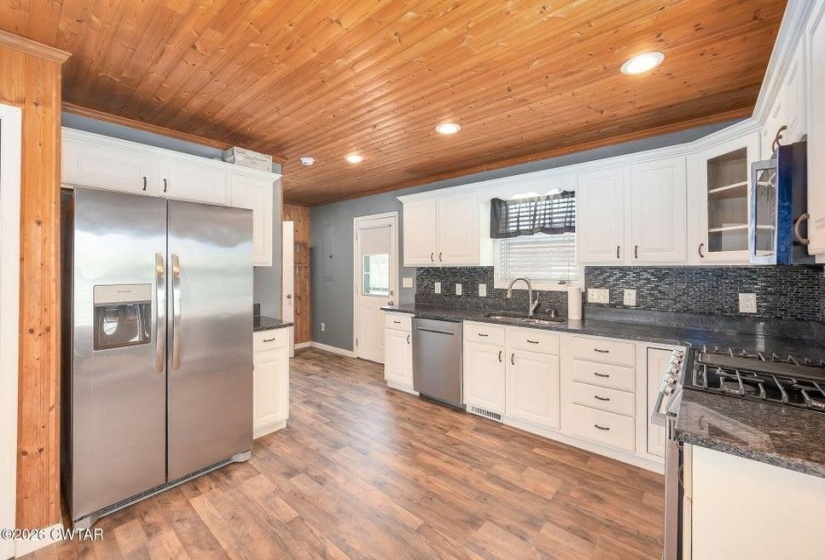 Kitchen featuring stainless steel appliances, white cabinetry, dark stone counters, wooden ceiling, and recessed lighting