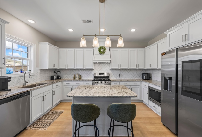 Kitchen featuring stainless steel appliances, light wood finished floors, light stone countertops, and a kitchen island