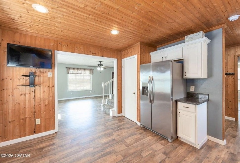 Kitchen with stainless steel fridge with ice dispenser, white cabinetry, dark wood finished floors, wood walls, and recessed lighting
