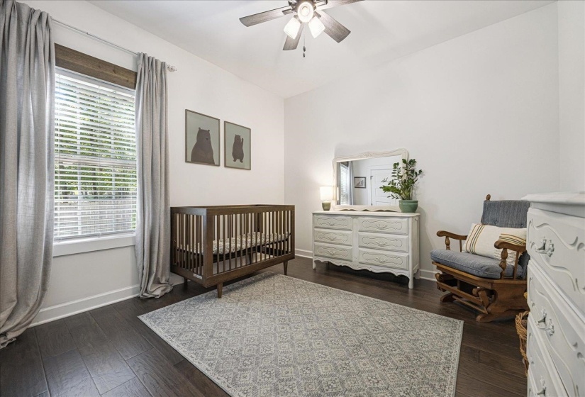 Bedroom with dark wood-style floors, a nursery area, and ceiling fan