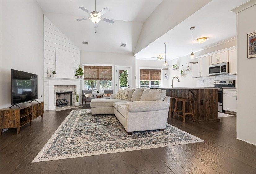 Living area with a fireplace, dark wood-style floors, high vaulted ceiling, and a ceiling fan