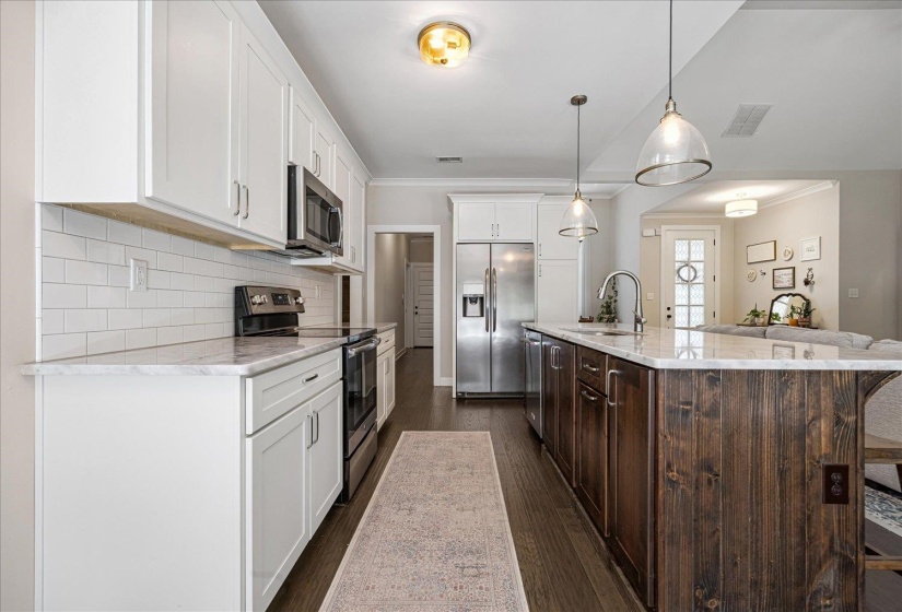 Kitchen with stainless steel appliances, hanging light fixtures, white cabinetry, dark wood-style floors, and crown molding