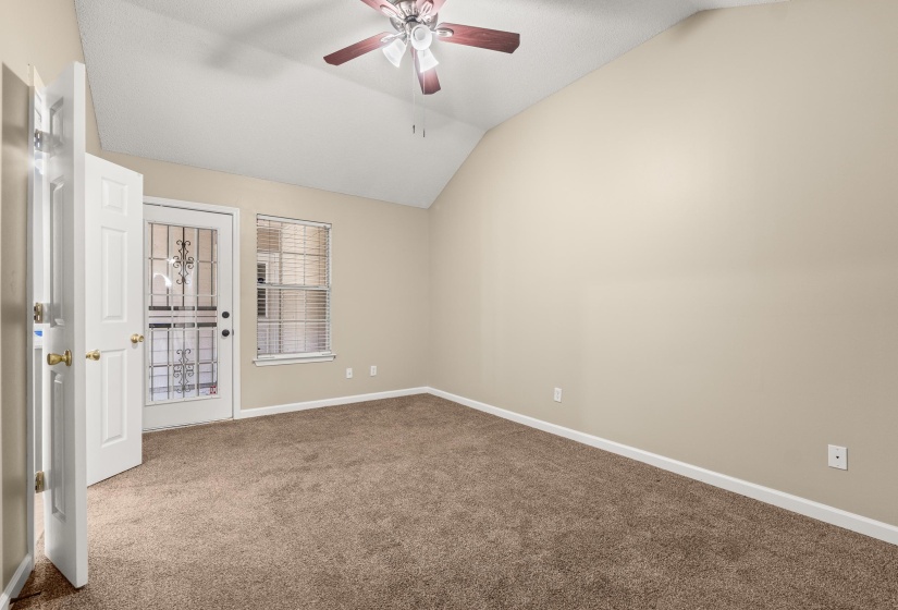 Vaulted ceiling room featuring neutral-toned walls, brown carpet, white trim, and a ceiling fan