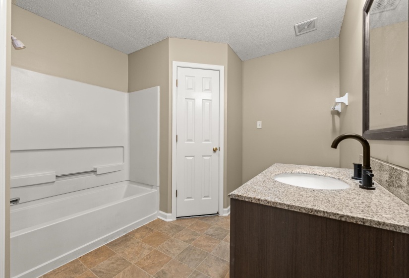 Bathroom featuring a white tub and shower surround, a vanity with a light-colored speckled countertop, an undermount sink, and a dark bronze gooseneck faucet