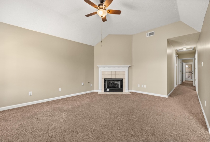 Spacious living area featuring vaulted ceilings, a central fireplace with a tile surround and white mantel, and a ceiling fan with light fixture