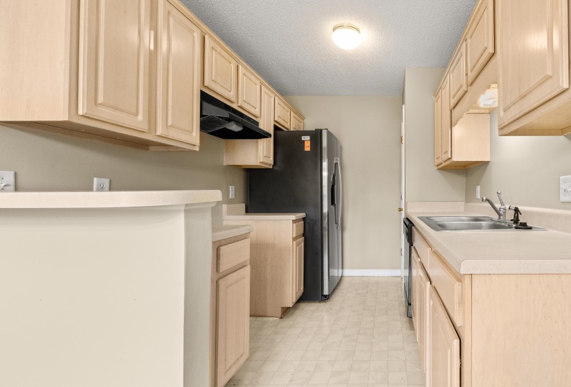 Galley kitchen featuring light wood cabinetry, laminate countertops, a double basin stainless steel sink, and a black appliance suite