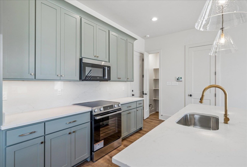 Kitchen with stainless steel appliances, light stone counters, dark wood-style floors, backsplash, and pendant lighting