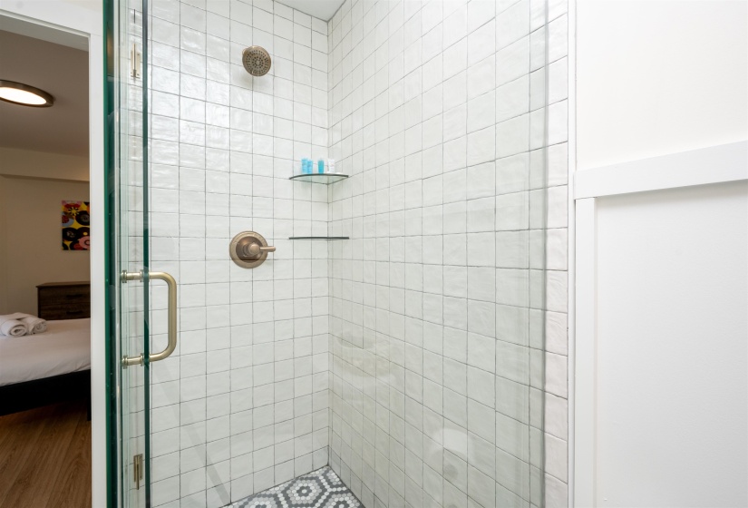 Tiled shower stall featuring a clear glass enclosure, bronze-finish fixtures, white square wall tile, and a geometric pattern floor tile
