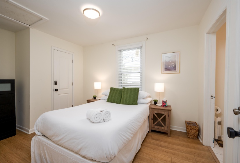 Bedroom featuring wood-finish flooring, a ceiling-mounted light fixture, and a window with horizontal blinds