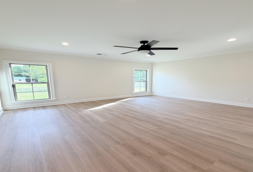 Spacious room featuring light wood-finish flooring, two large windows, a black ceiling fan, recessed lighting, and crown molding