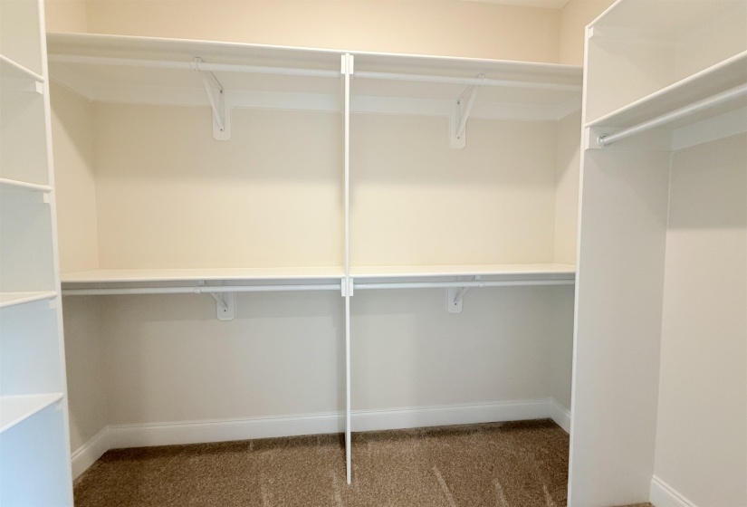 Walk-in closet featuring white built-in shelving, multiple hanging rods, and light-colored carpet flooring
