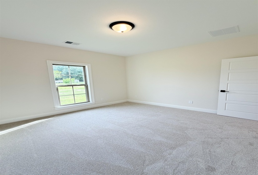 Neutral tone carpet flooring, white painted walls, and a white interior door with matte black hardware