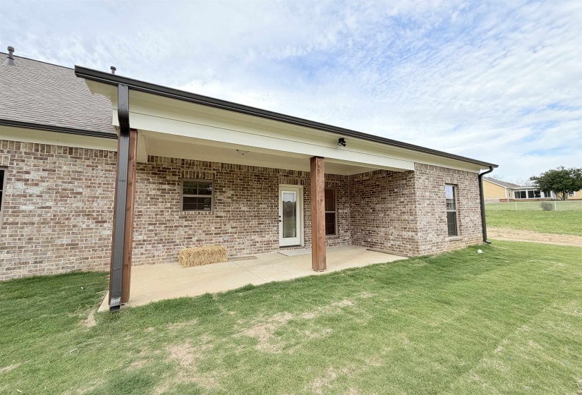 Covered concrete patio featuring two wood support columns, brick exterior, and dark brown gutters