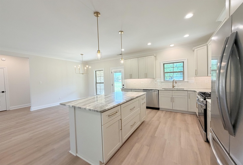 Contemporary kitchen featuring an island with a stone countertop, light wood-finish flooring, white cabinetry, stainless steel appliances, and recessed lighting