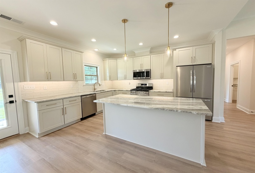 Kitchen featuring light wood-finish flooring, white perimeter cabinetry, stainless steel appliances, and a central island with a stone-finish countertop