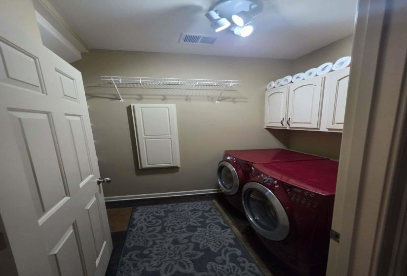 Dedicated laundry space featuring upper cabinetry, a wall-mounted drying rack, and track lighting. A hidden ironing board and multiple shelves