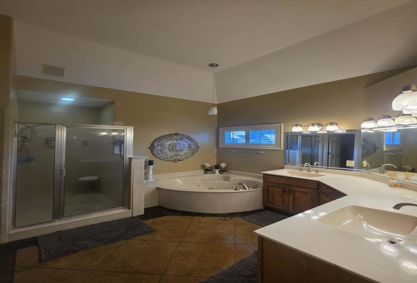 Bathroom featuring a corner jetted tub, a separate glass-enclosed shower, dual vanity with undermount sinks, and a vaulted ceiling