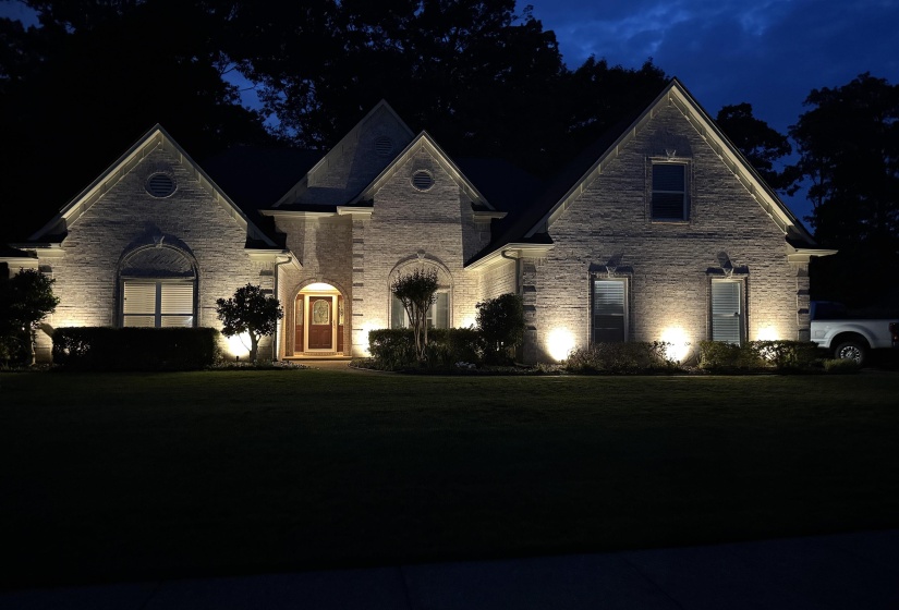 Brick exterior with arched entry, illuminated by integrated landscape lighting