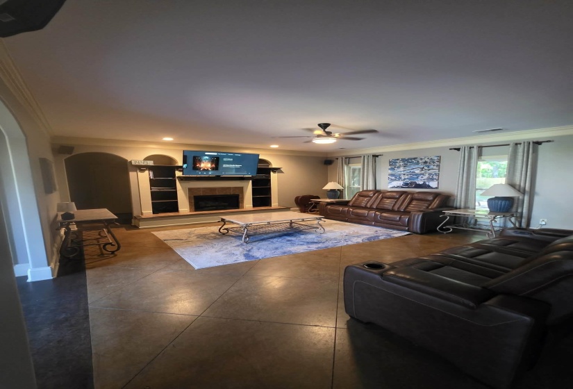 Spacious living area featuring sealed concrete flooring, a fireplace with integrated shelving, recessed lighting, and a ceiling fan