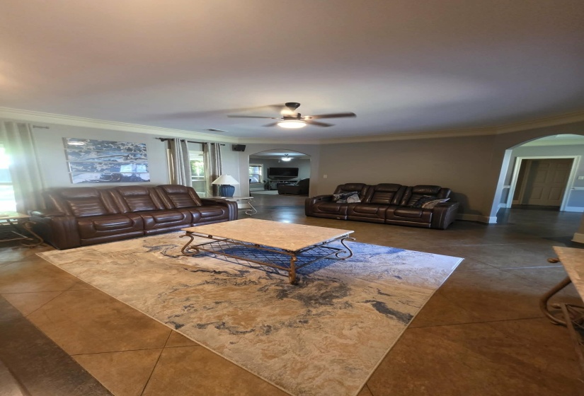 Spacious living area featuring large format tile flooring, crown molding, and a ceiling fan with integrated lighting