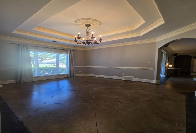 Spacious room featuring a tray ceiling with crown molding, an ornate chandelier, and large window with blinds