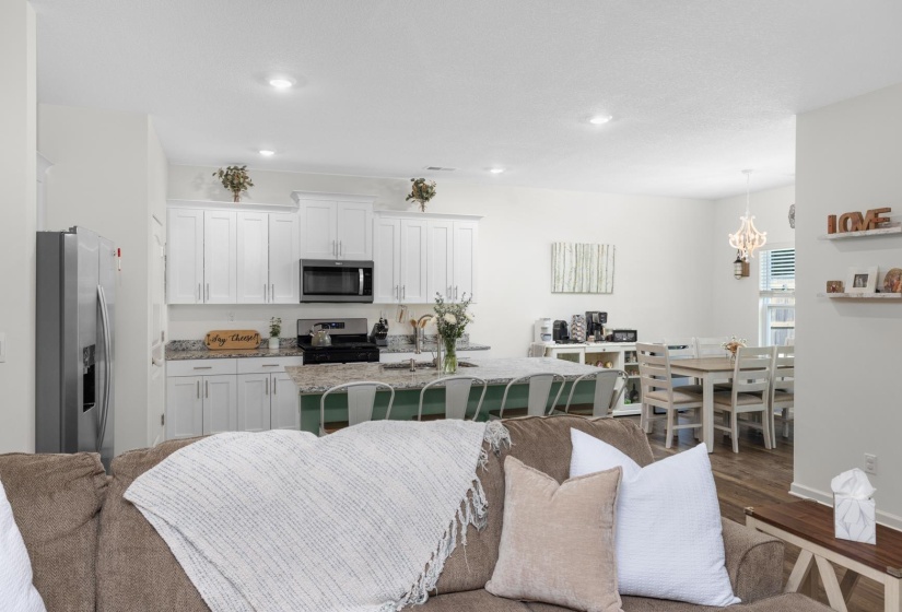 Open-concept living space featuring a modern kitchen with white cabinetry, granite countertops, and stainless steel appliances