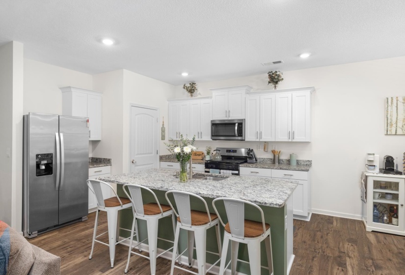 Modern kitchen featuring a central island with seating, white shaker-style cabinetry, stainless steel appliances, and wood-finish flooring