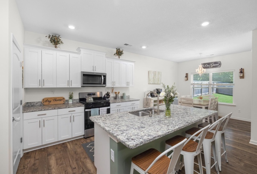 Bright kitchen featuring a substantial island with integrated sink, white cabinetry with brushed nickel hardware, stainless steel appliances, and wood-finish flooring