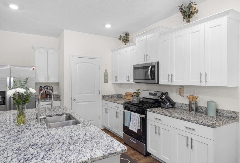 Modern kitchen featuring a large island with an undermount double-basin sink, granite countertops, white shaker cabinetry, stainless steel appliances, and recessed lighting
