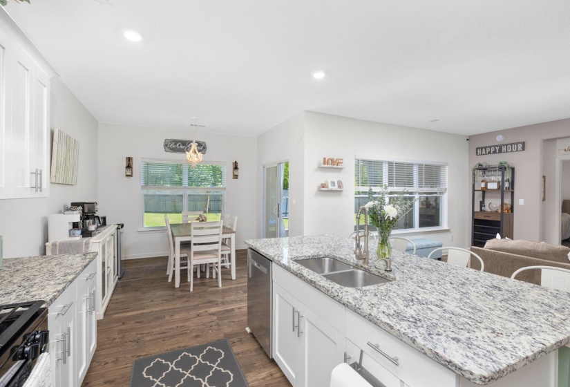 Kitchen featuring granite countertops, a double basin stainless steel sink with gooseneck faucet, white shaker cabinetry with brushed nickel hardware, stainless steel appliances, and wood-finish flooring