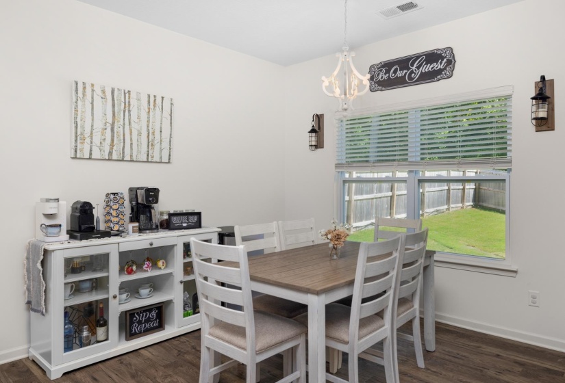 Dining area featuring wood-finish flooring, a contemporary white chandelier, dual wall-mounted sconces, and a large window overlooking a fenced backyard