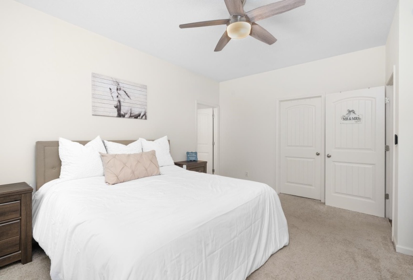 Carpeted room featuring a ceiling fan with light fixture, light-toned walls, and white paneled doors