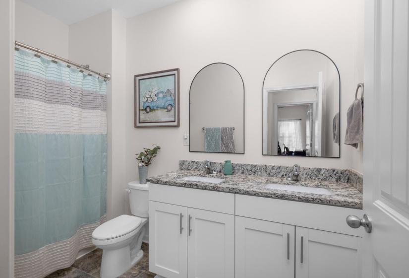 Bathroom featuring a dual vanity with a patterned countertop, two arched mirrors, white cabinetry with silver hardware, and a tub/shower combination